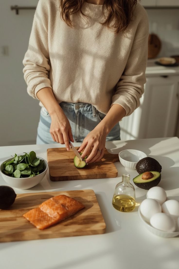 Mujer cortando aguacate en una tabla de madera, con salmón, espinacas y huevo sobre la barra