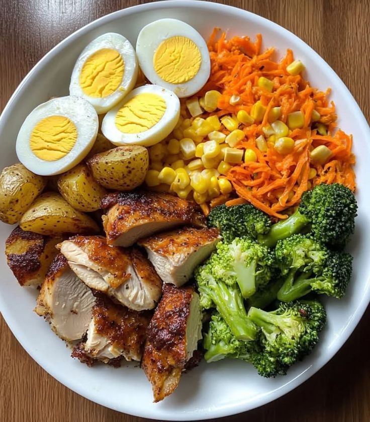 Plato con trozos de pollo asado, huevo cocido, papas, brócoli, elote y zanahoria rallada